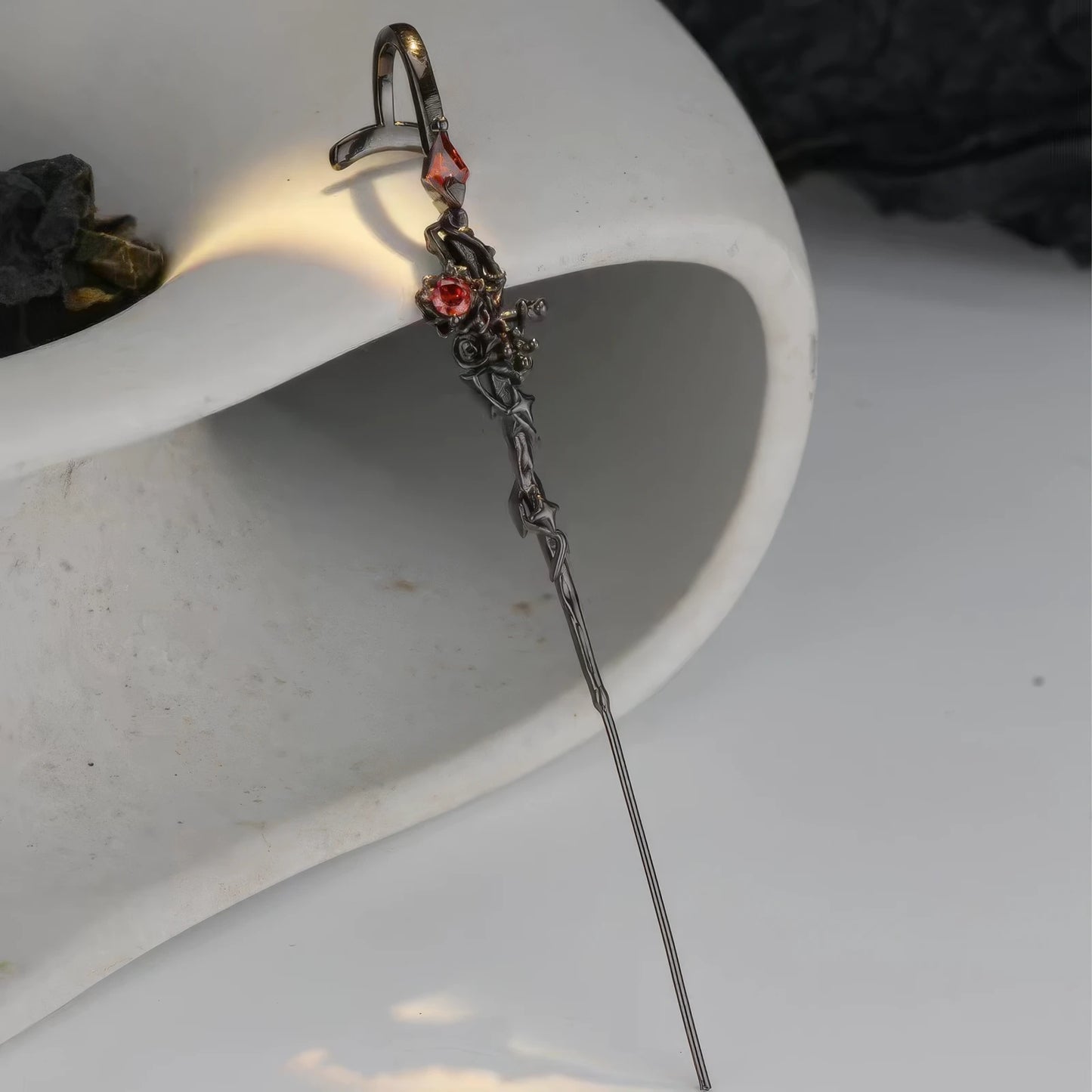 Black rose piercing ear cuff placed on a white curved surface, showing the side view.
