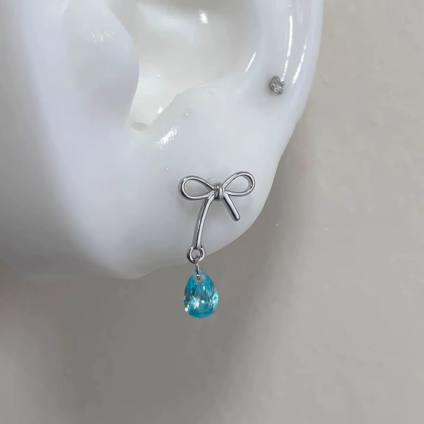 Bow - shaped blue diamond earrings displayed on a white ear model, showing the design clearly.