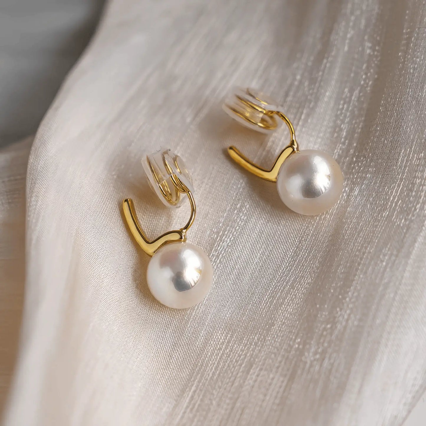 Colorful pearl spiral clip earrings placed on light fabric, emphasizing the delicate design and pearl luster
