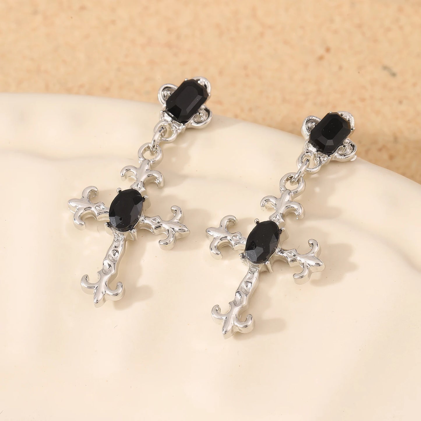 Dark gem cross earrings displayed on a white plate
