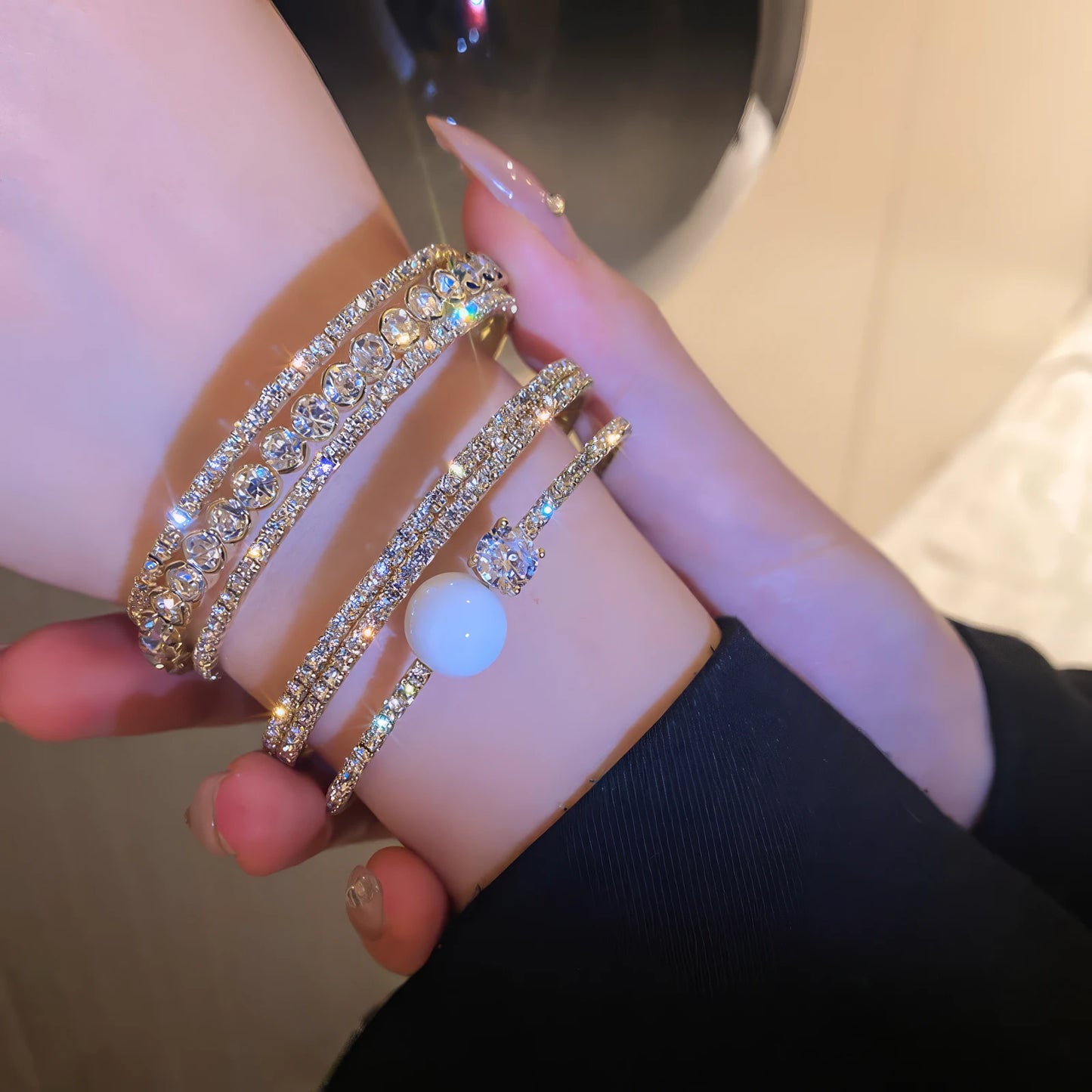 Diamond - inlaid open bracelet with pearl detail worn on wrist, stacked with other bracelets.