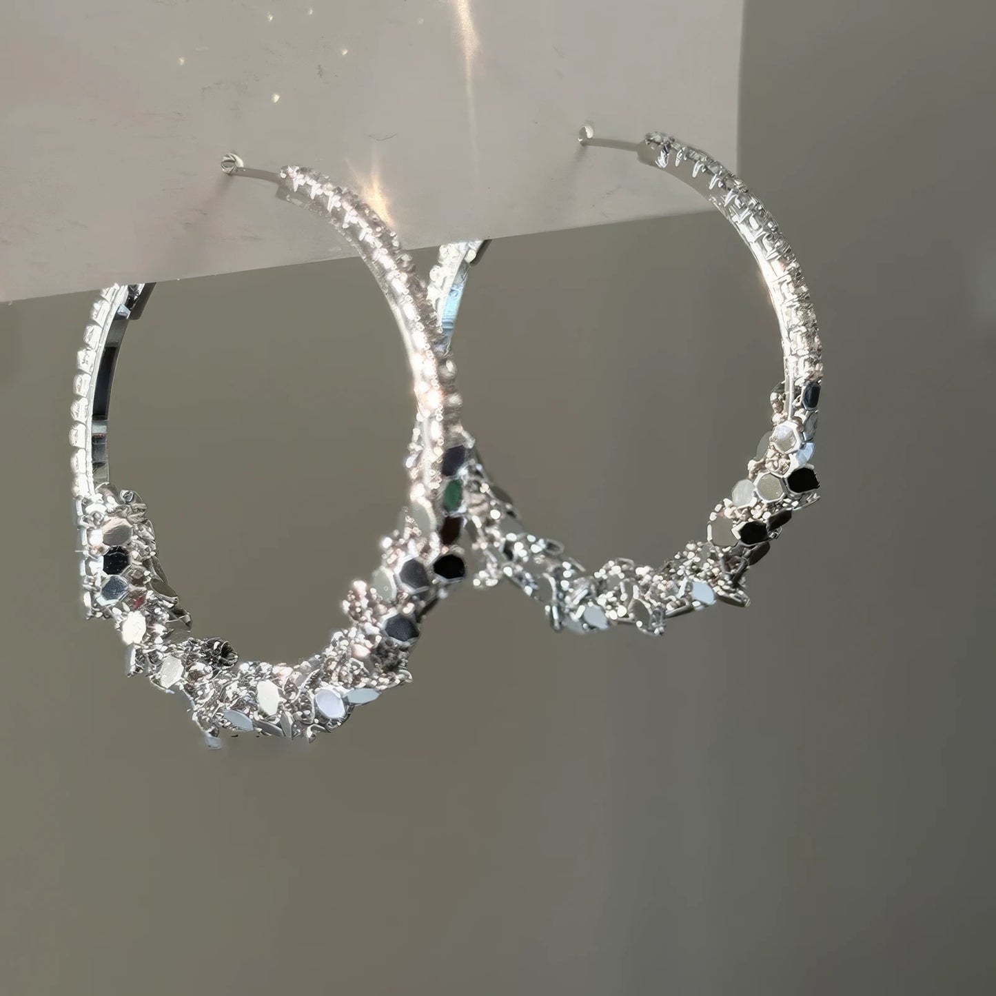 Pair of diamond - inlaid round hoop earrings, hanging and displayed, showcasing the sparkling stone - encrusted design with a mix of clear and dark stones