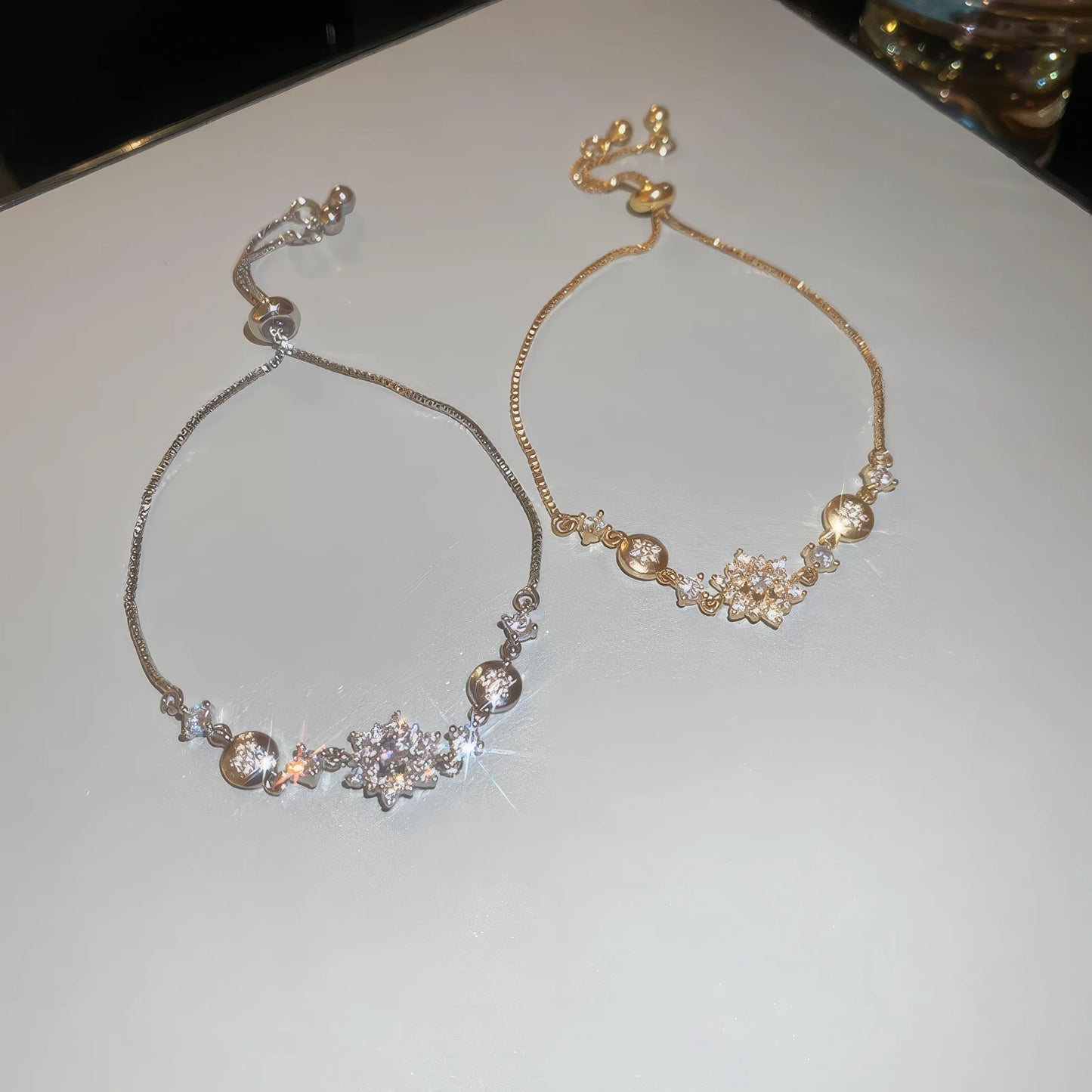 Pair of diamond - inlaid snowflake pendant bracelets (silver and gold) on light background.