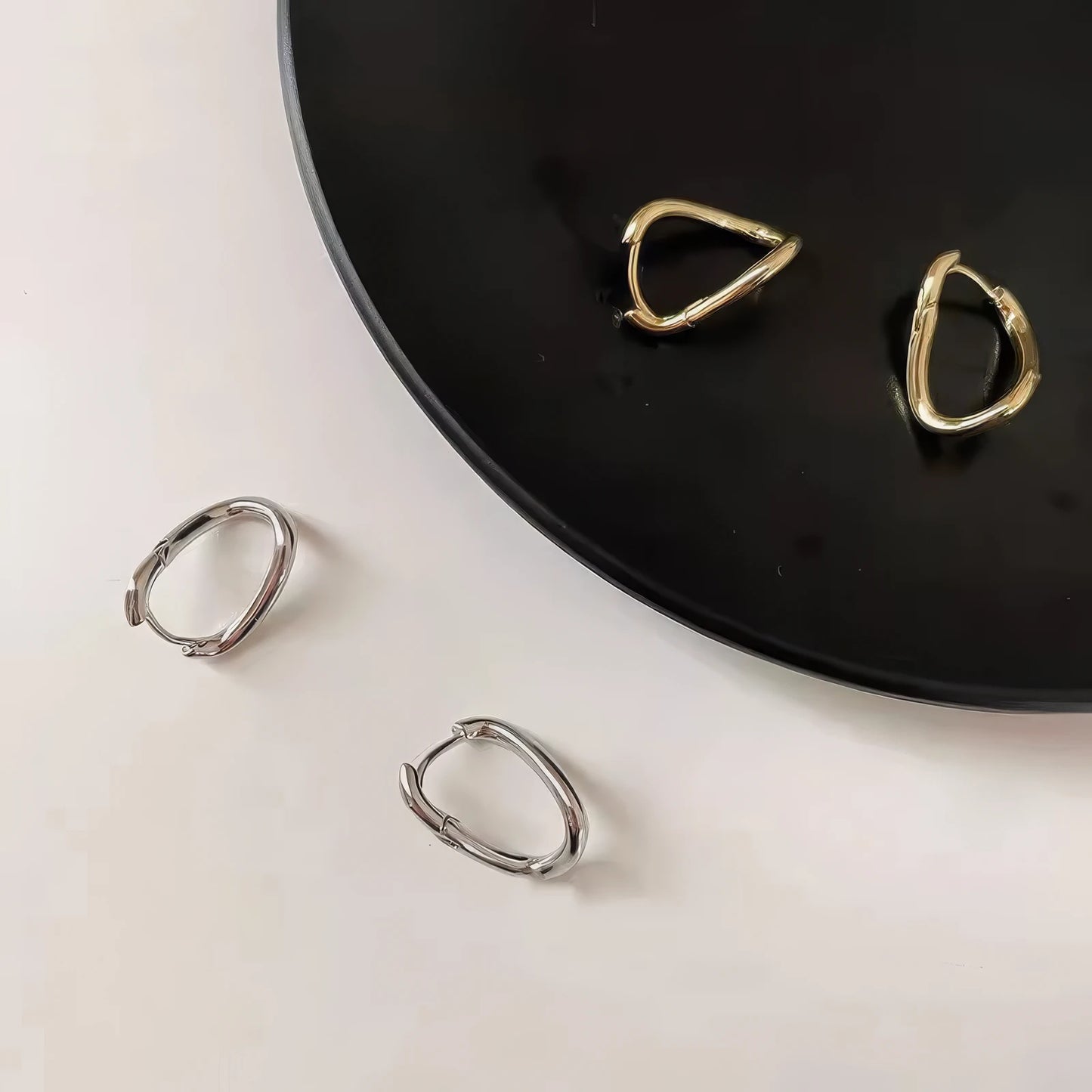 Mixed gold and silver geometric irregular silver needle earrings, displayed on a black and white surface, emphasizing the contrast of metallic tones and unique shapes.