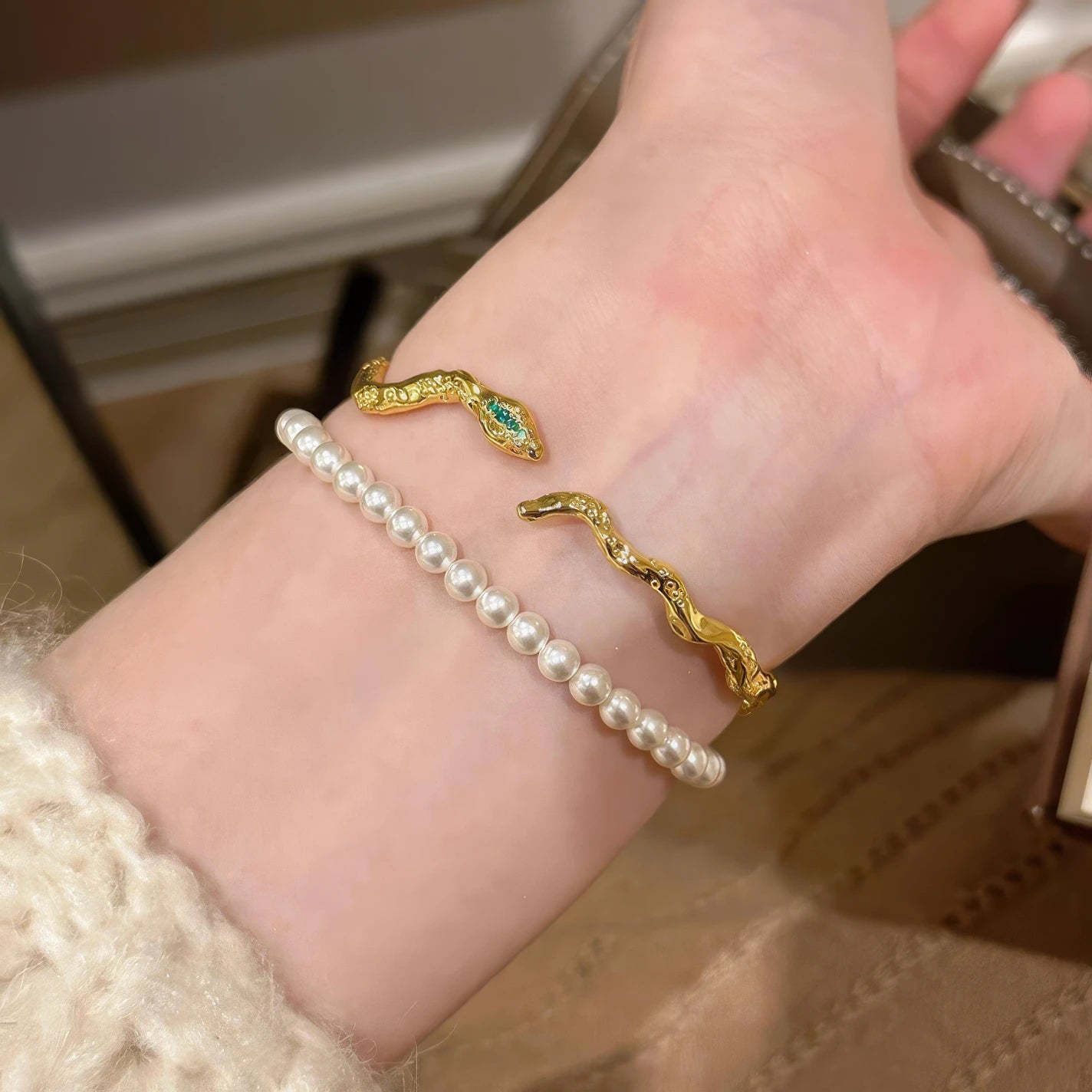Gold - toned popular snake - shaped bracelet stacked with a pearl bracelet, worn on wrist.