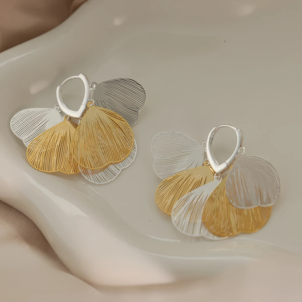Pair of mixed gold and silver hollow petal - shaped tassel earrings, displayed on a curved surface, showcasing the contrast of metallic tones