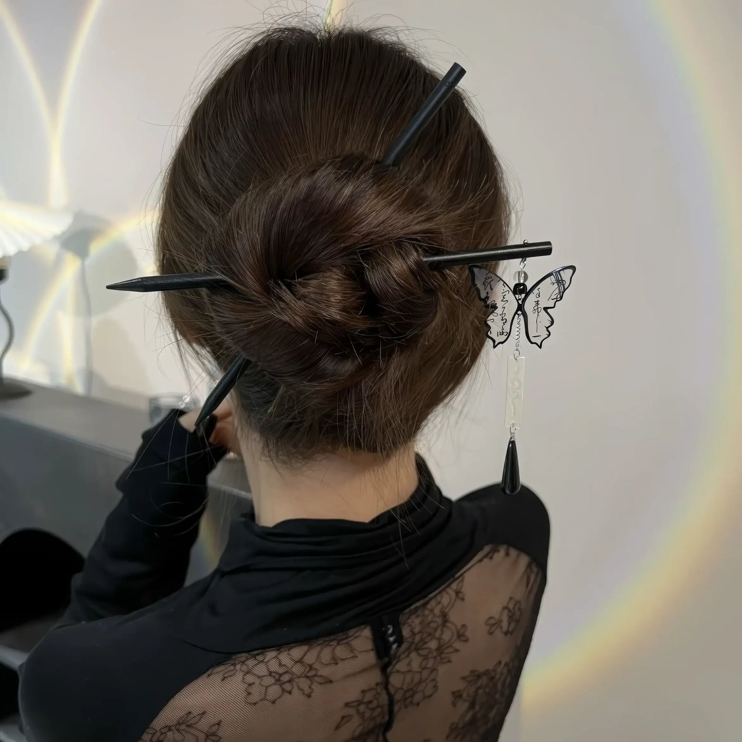 Ink - wash butterfly black sandalwood hairpin worn in a bun, viewed from the back, with a sheer - patterned top.