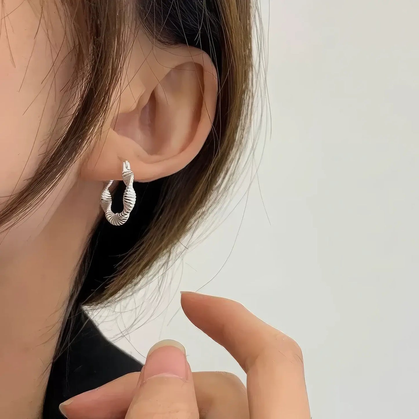 Silver minimalist twisted hoop earring worn, hand adjusting, highlighting the subtle, twisted structure on the ear