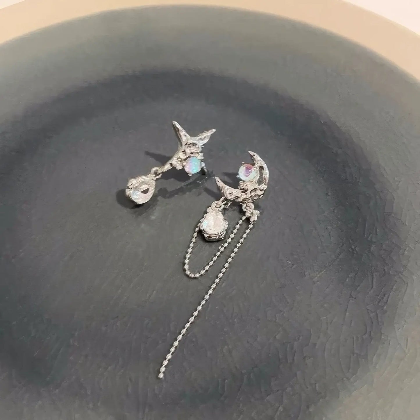 Moon and star asymmetric zircon earrings placed on a dark - colored surface, emphasizing the zircon details.