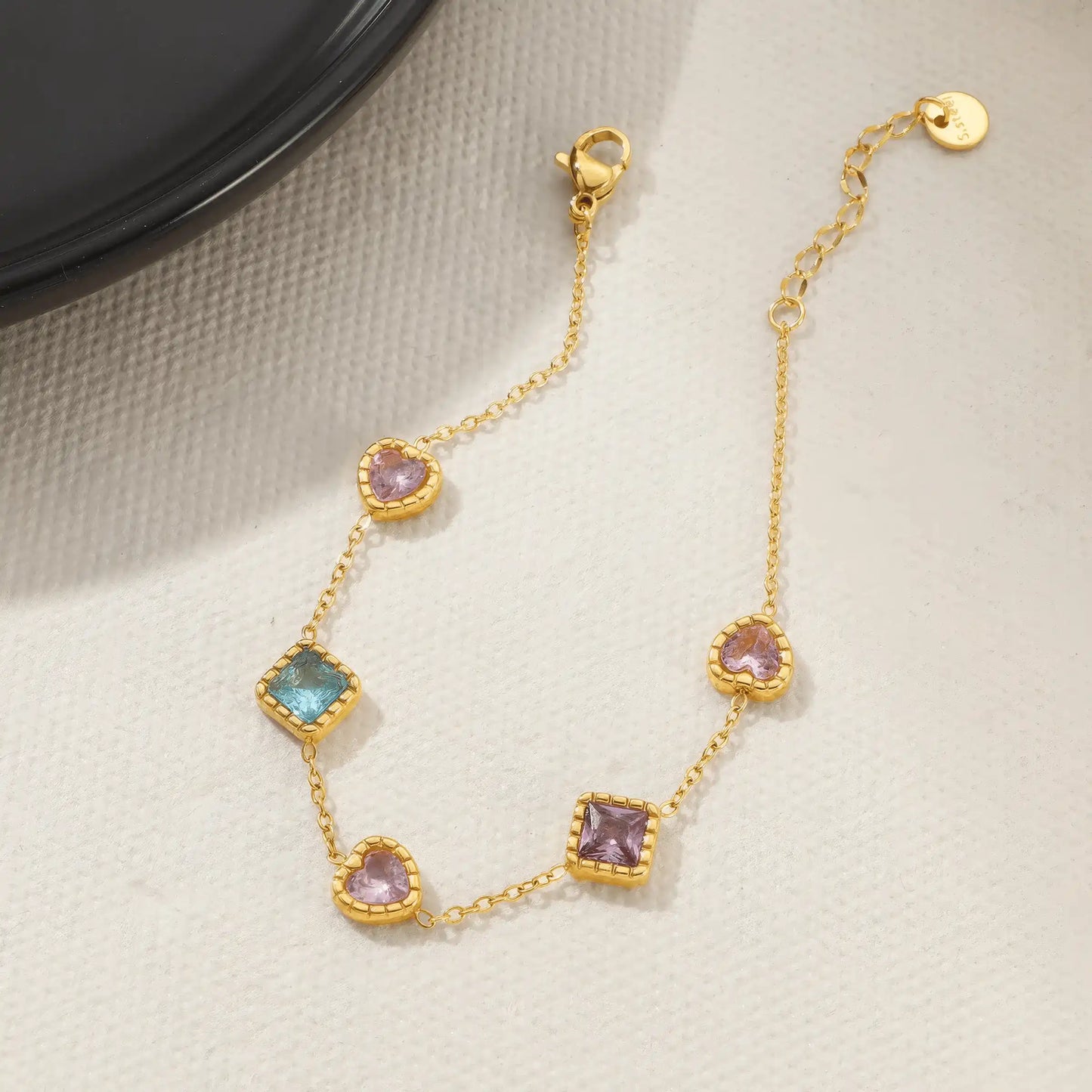 Multi - color zircon heart bracelet placed on light - colored fabric.