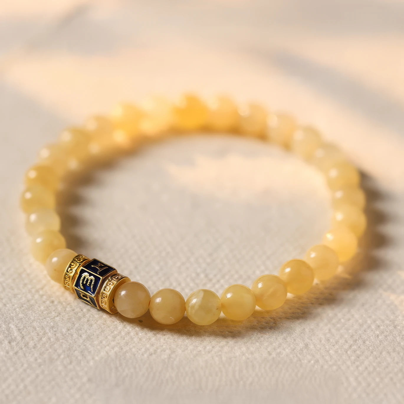 Natural cream - yellow jade bead bracelet with a decorative spacer bead, placed on a light - colored fabric surface.