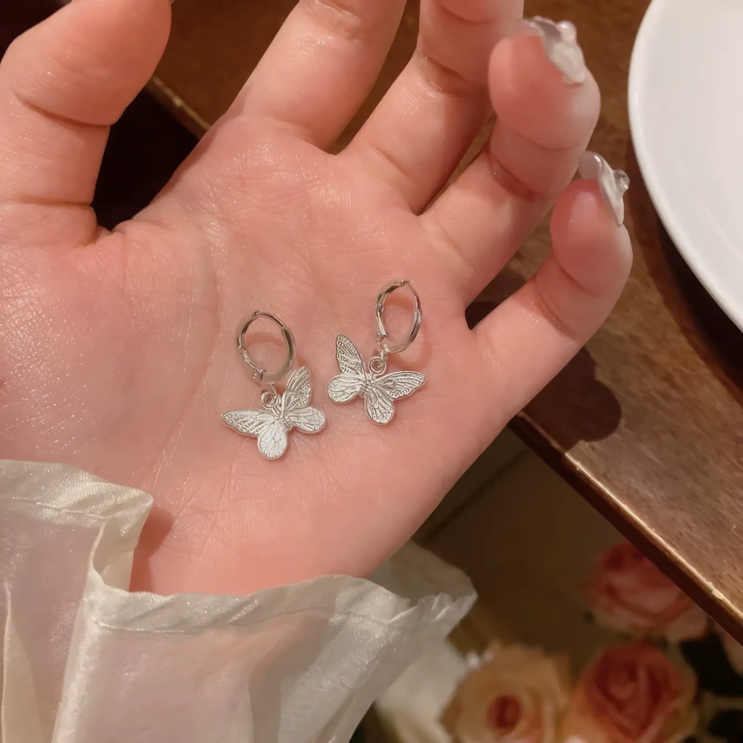 Pair of silver neo - Chinese style butterfly earrings held in a hand, showcasing the delicate, sparkling butterfly design.