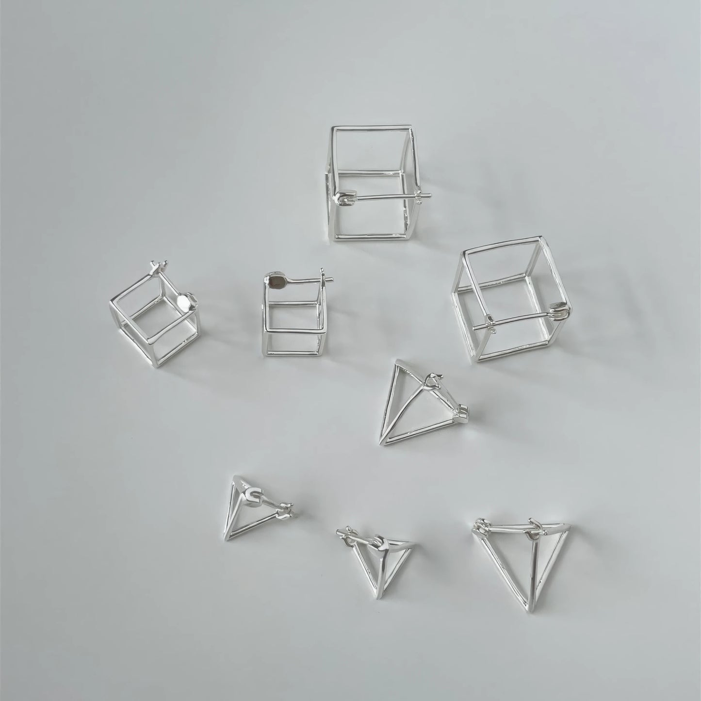 A collection of new geometric hollow earrings in various styles (triangle, cube, etc.), displayed on gray background, showcasing design variety.