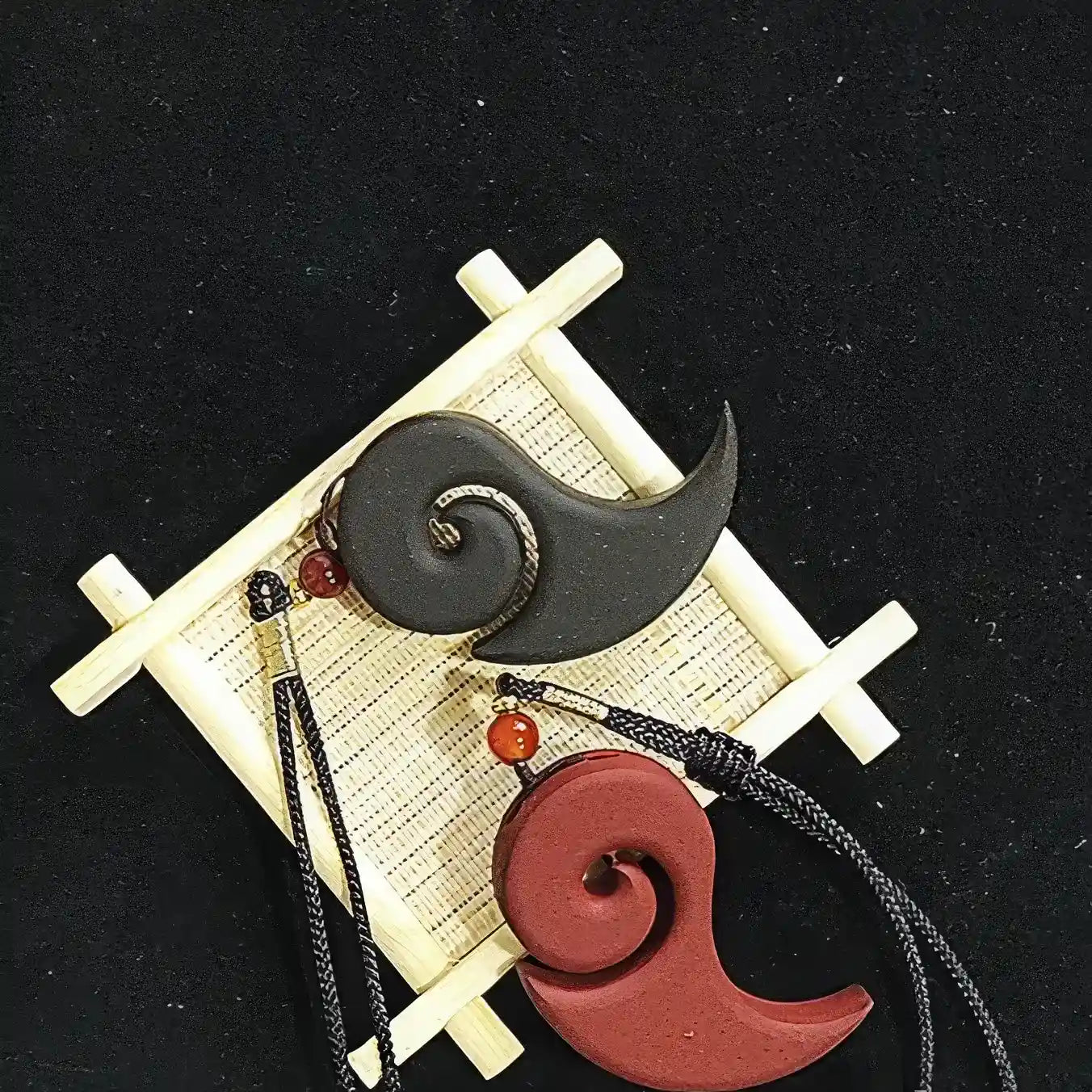 Red and dark - colored Nezha's Demon Pill incense pendants placed on a bamboo - themed background, showing the pendants' shape and the attached cords.