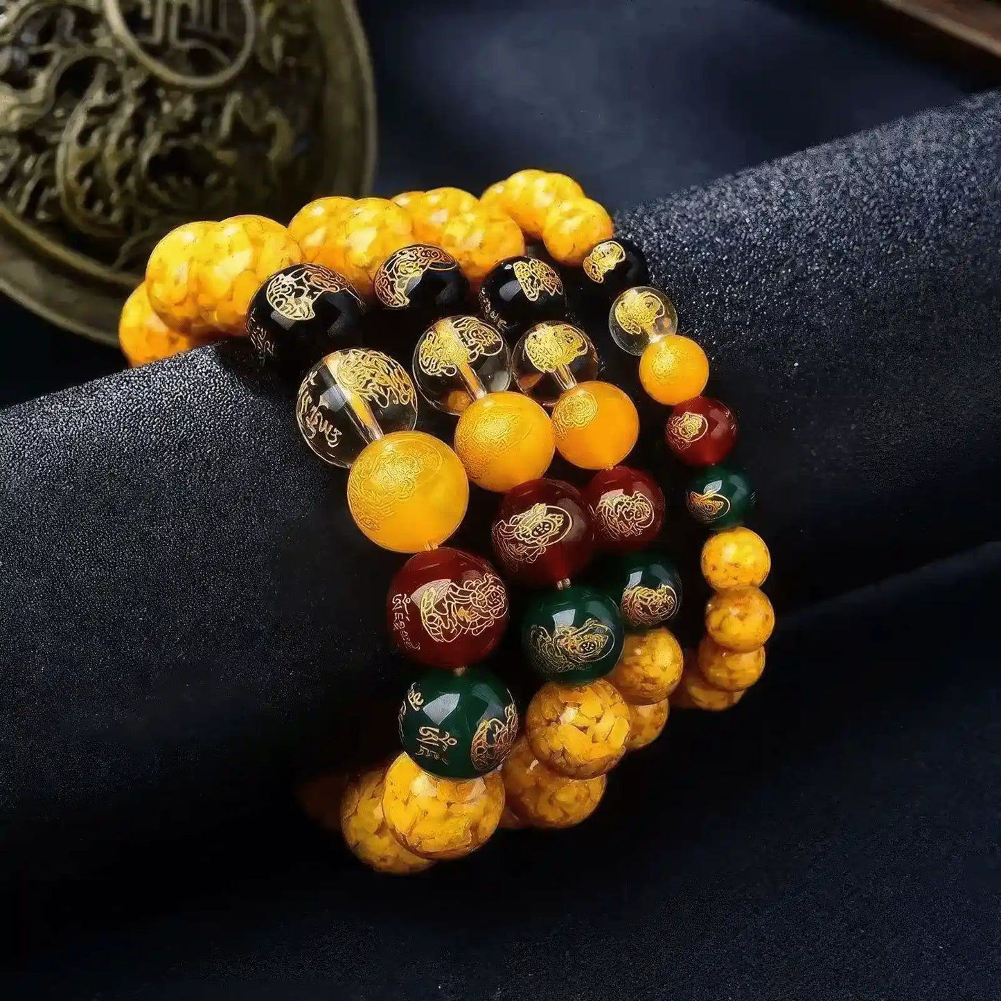 Multiple Pixiu Five - Way God of Wealth bracelets stacked together, showcasing yellow and red beads, on a dark fabric.