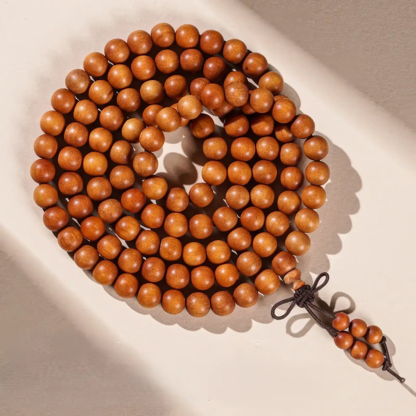 Another view of premium Laos sandalwood prayer beads coiled on a light - colored background.