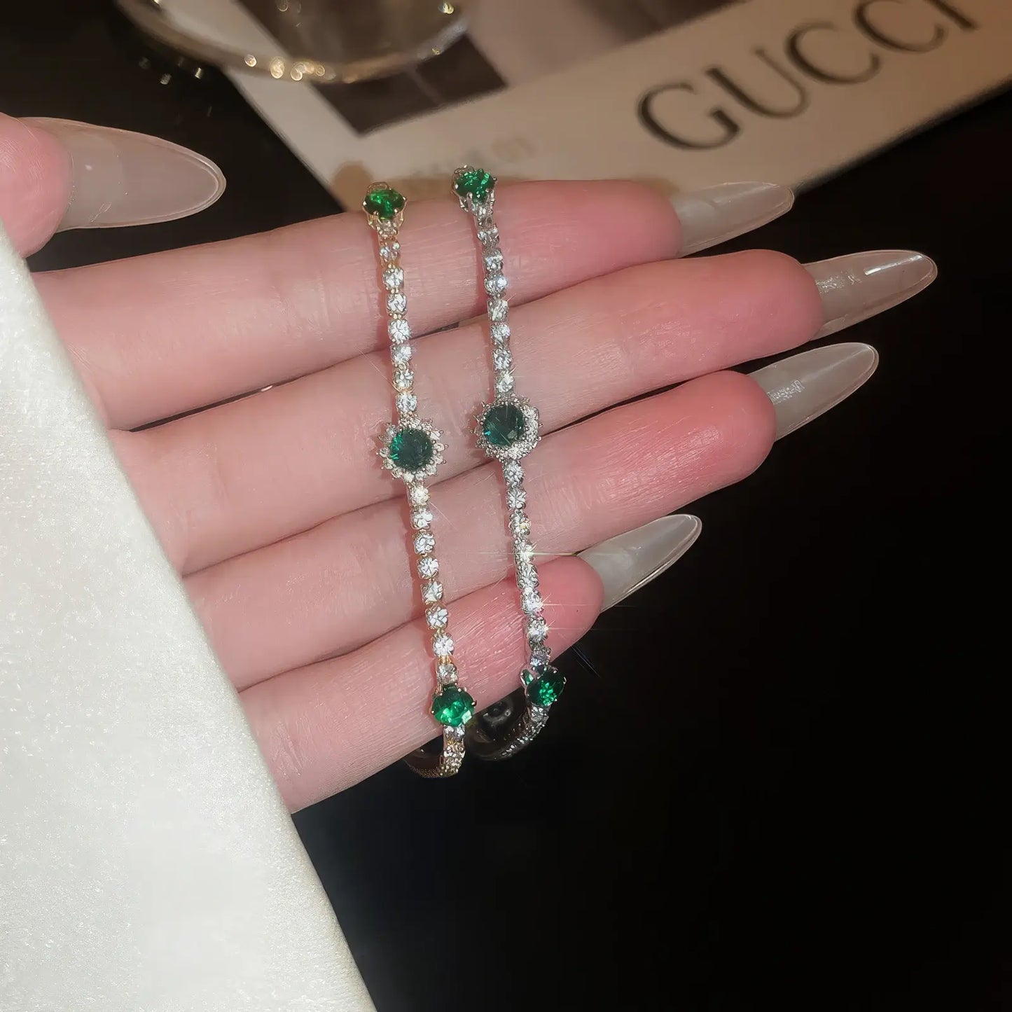 Pair of sea blue full diamond bracelets held in hand, with a "GUCCI" background.