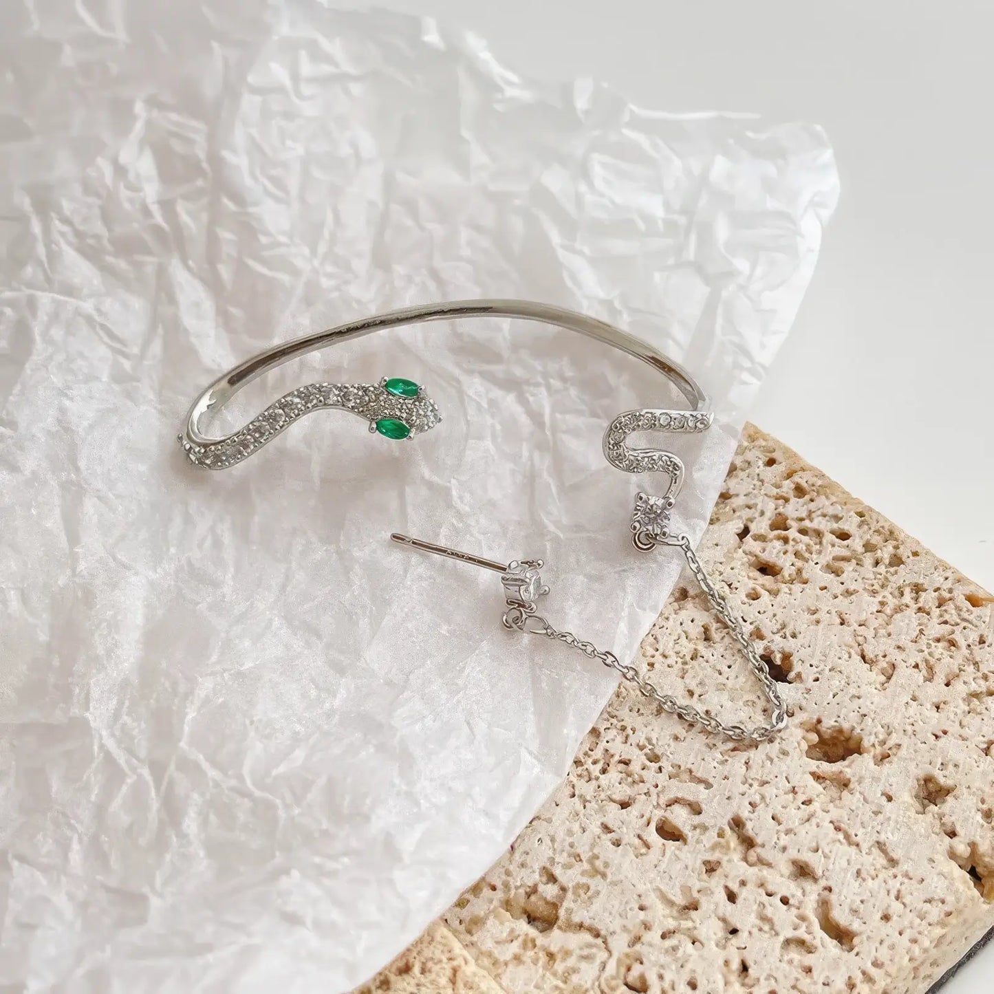 Silver needle diamond - inlaid snake - shaped ear cuff laid out on textured paper, showcasing the detailed and sparkling snake - shaped ear accessory.