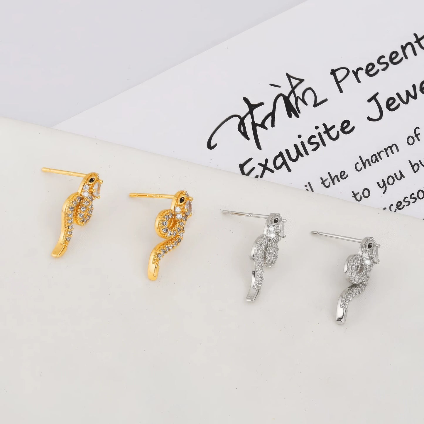 Mixed set of gold and silver snake - shaped stud earrings, displayed on a card with text, showcasing the variety of metallic tones