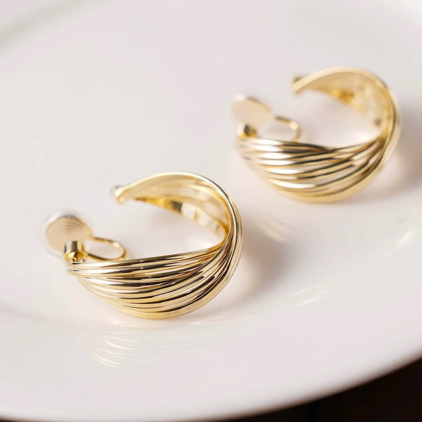 Gold textured line - ring ear cuffs displayed on a white plate, showcasing the reflective, layered design