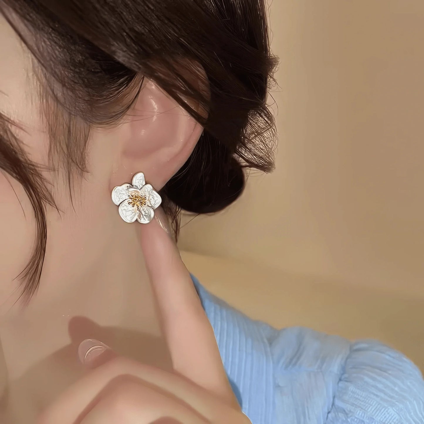 Two - tone new flower earring worn, finger pointing to it, emphasizing the minimalist yet elegant floral look