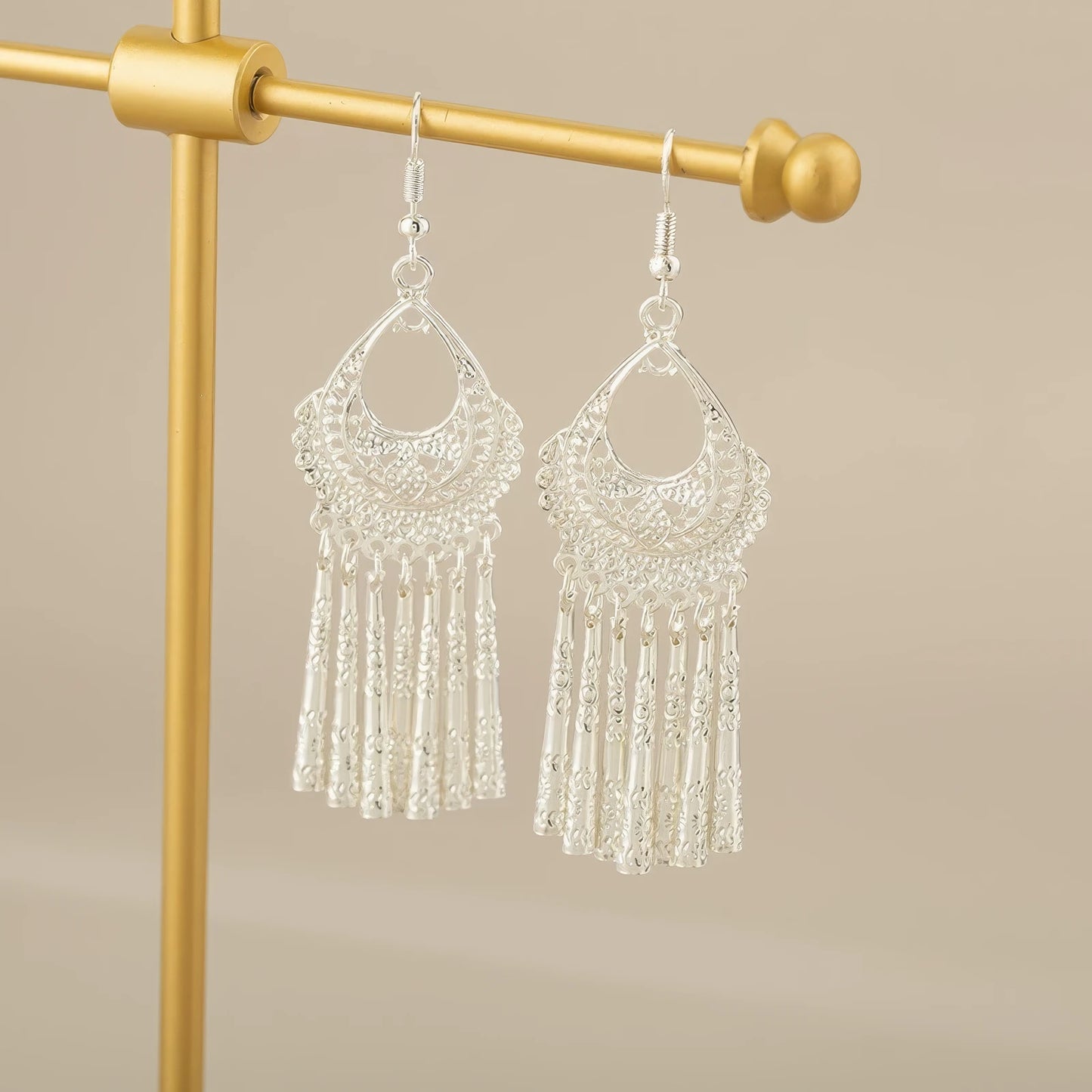 Water drop tassel Miao - Jiang style ear clips displayed on a gold - colored stand, highlighting the detailed and stylish silver - woven design with dangling tassels.
