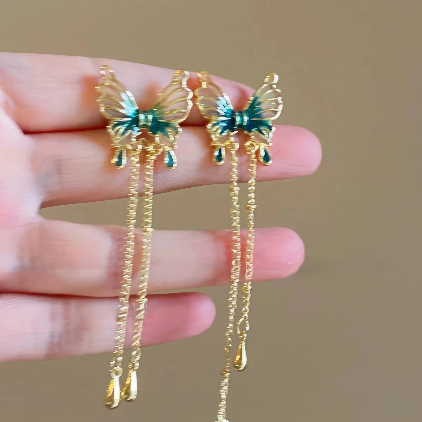Blue green butterfly dangle earrings held by fingers