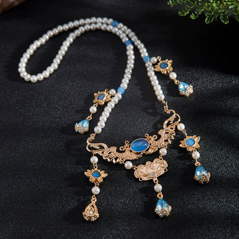 Detail of blue pendant necklace with pearls and gold details, displayed on dark background, full view