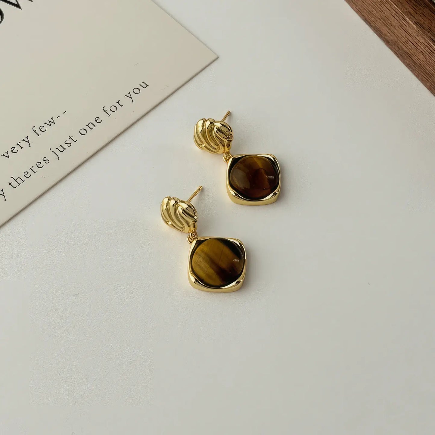 Brown tiger eye stone earrings, gold - tone, displayed on white pad with paper detail