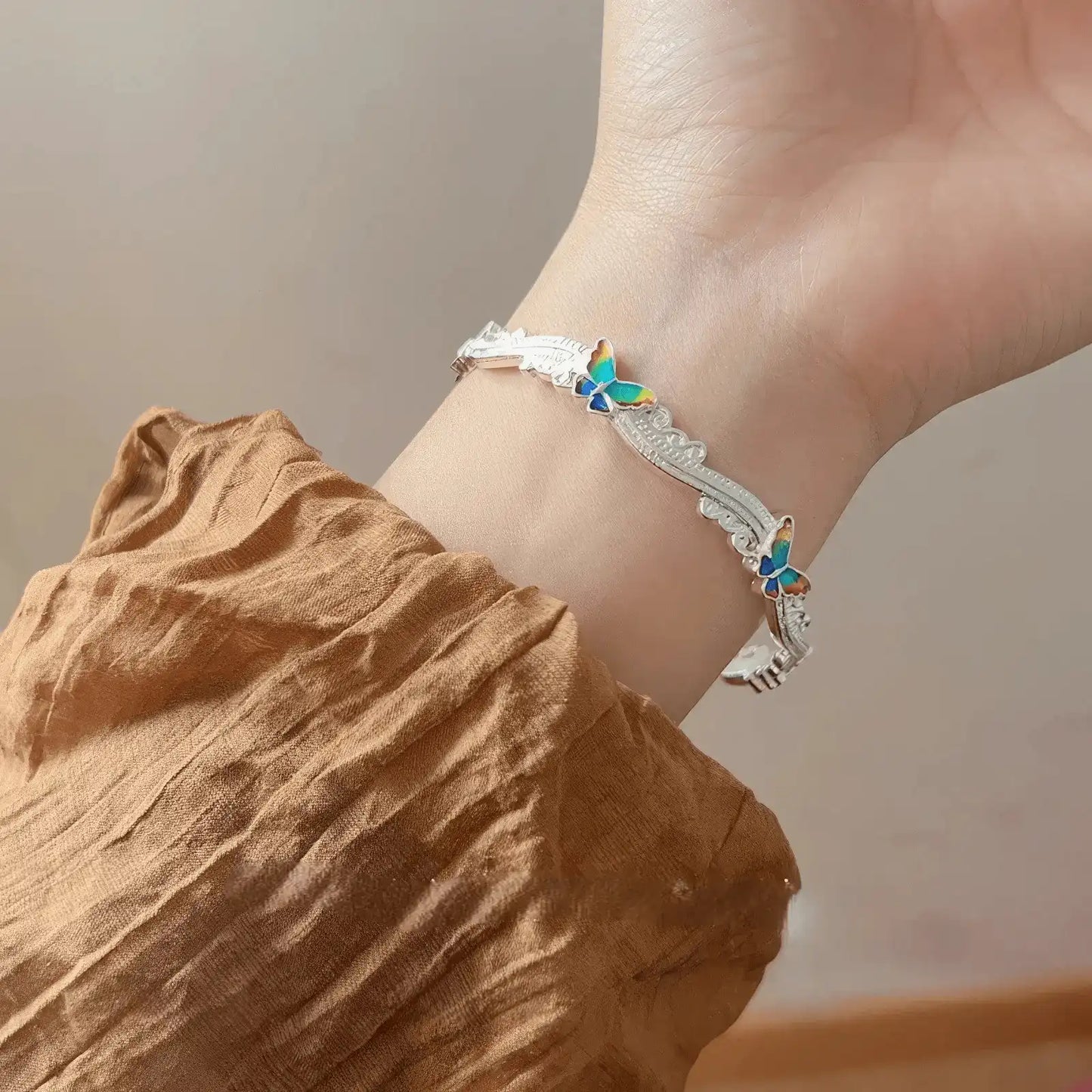 Another view of butterfly enamel oil - drop bangle worn on a wrist, brown sleeve background