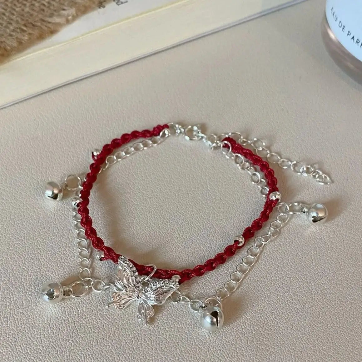 Butterfly red string bell bracelet isolated on light surface
