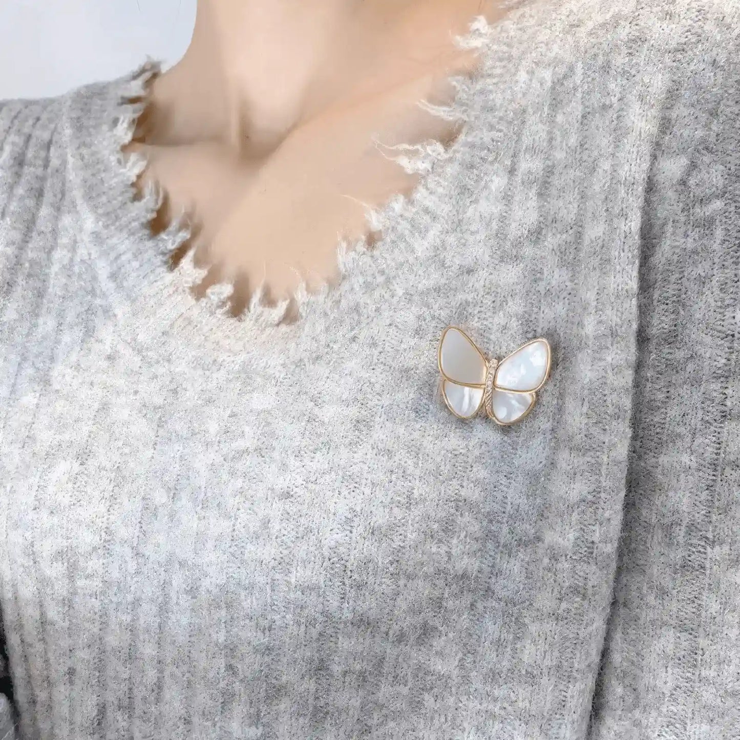Another angle of white butterfly brooch worn on gray sweater, emphasizing charm