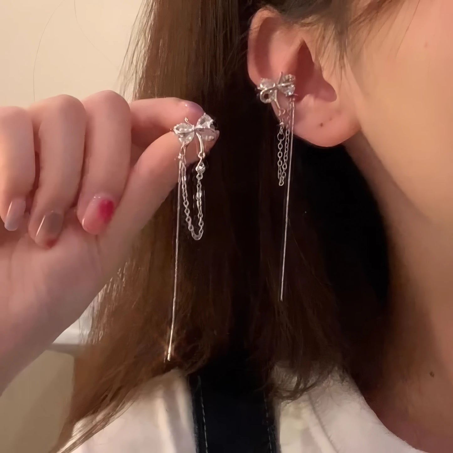 Hand putting on silver butterfly zircon ear cuff with tassel, showcasing delicate design