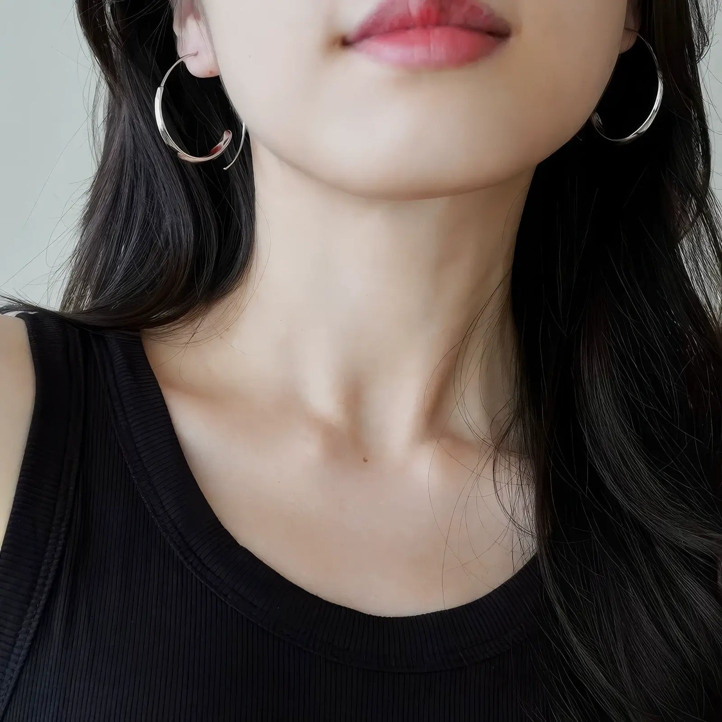 Pair of silver circle hoop earrings worn on ears, model in dark outfit, highlighting symmetry