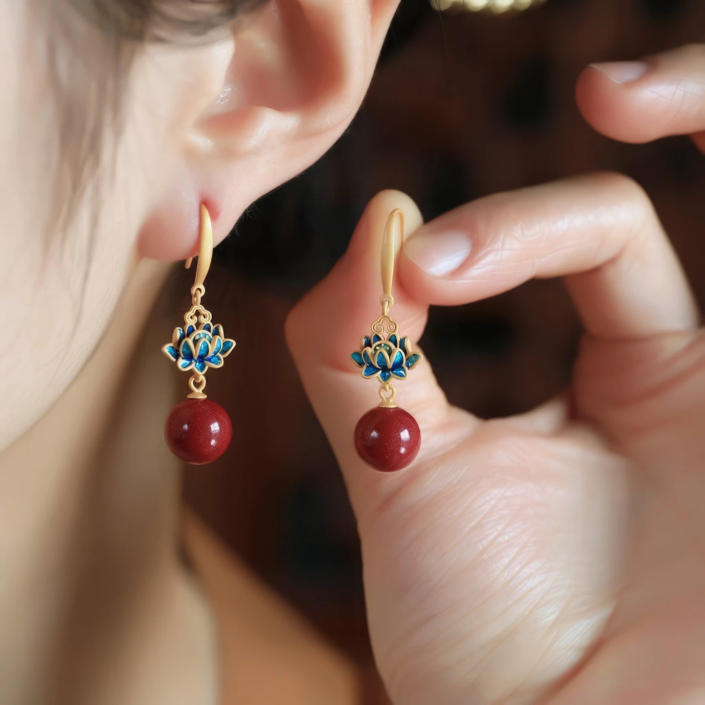 Cloisonne enamel cinnabar bead earrings, being adjusted on ear, showcasing blue floral detail