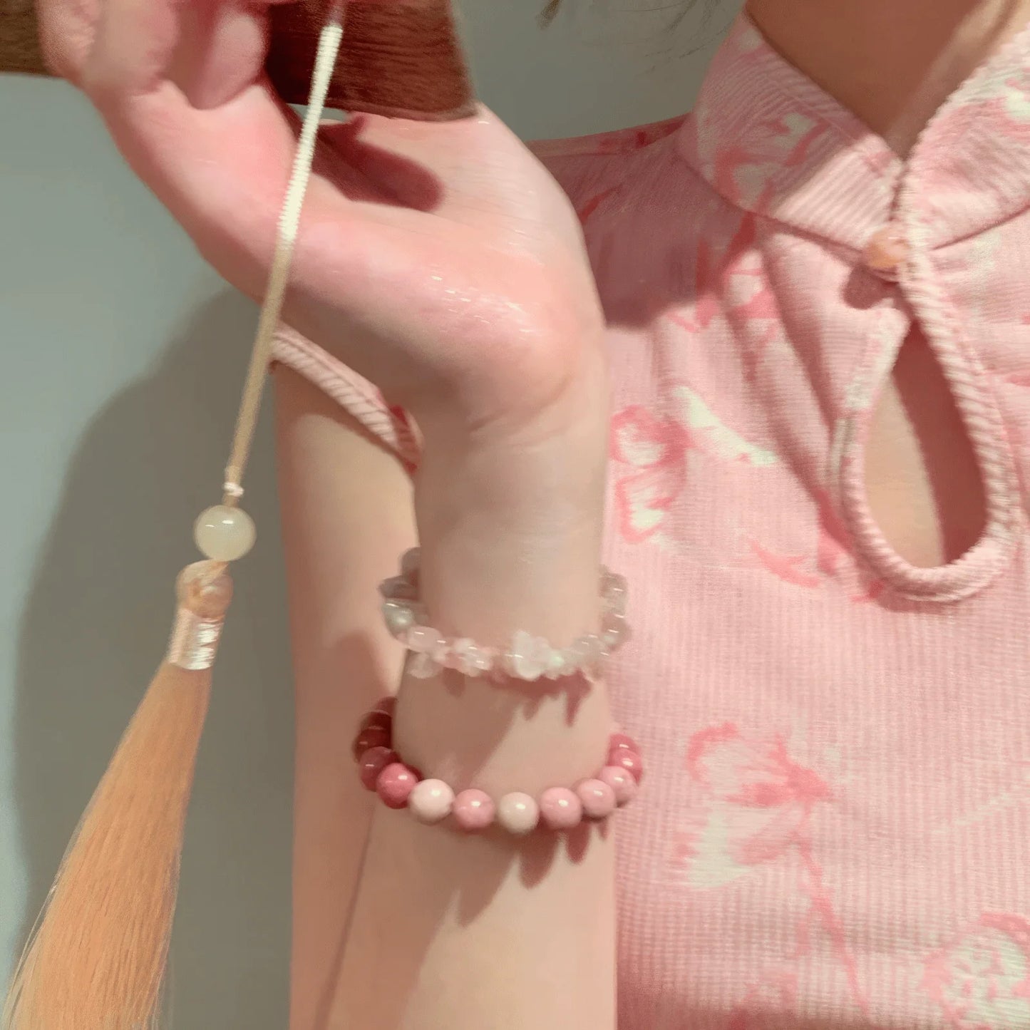 Hands wearing cloud - mountain neo - Chinese beaded bracelets, holding a tassel, pink cheongsam background