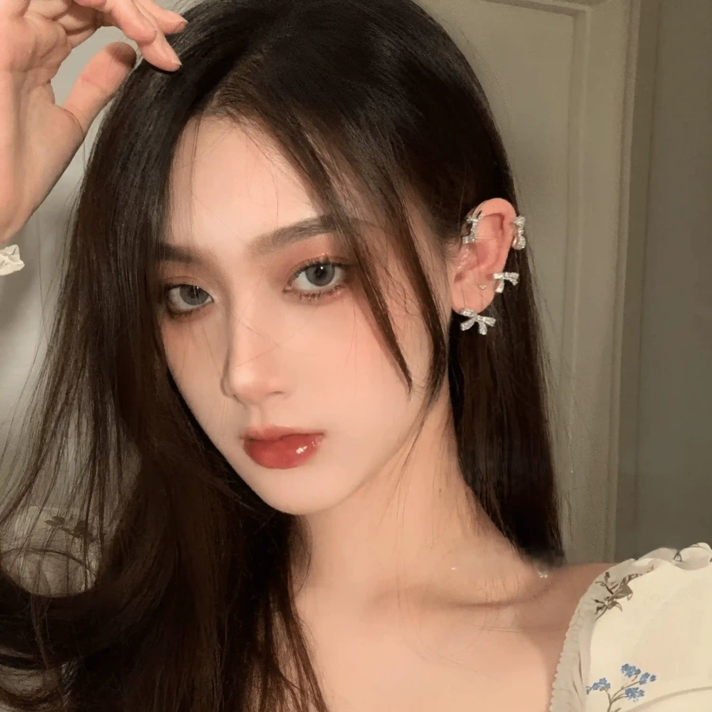 Silver diamond - encrusted bow ear cuff worn, full - face view of model