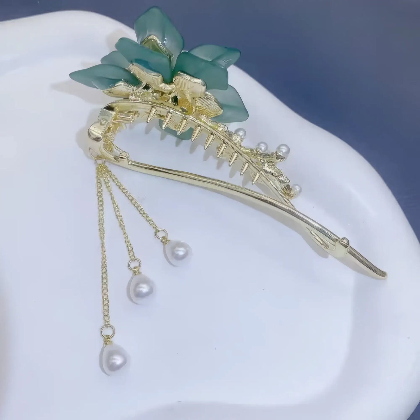 Side view of green flower butterfly tassel twist clip with pearls on white plate