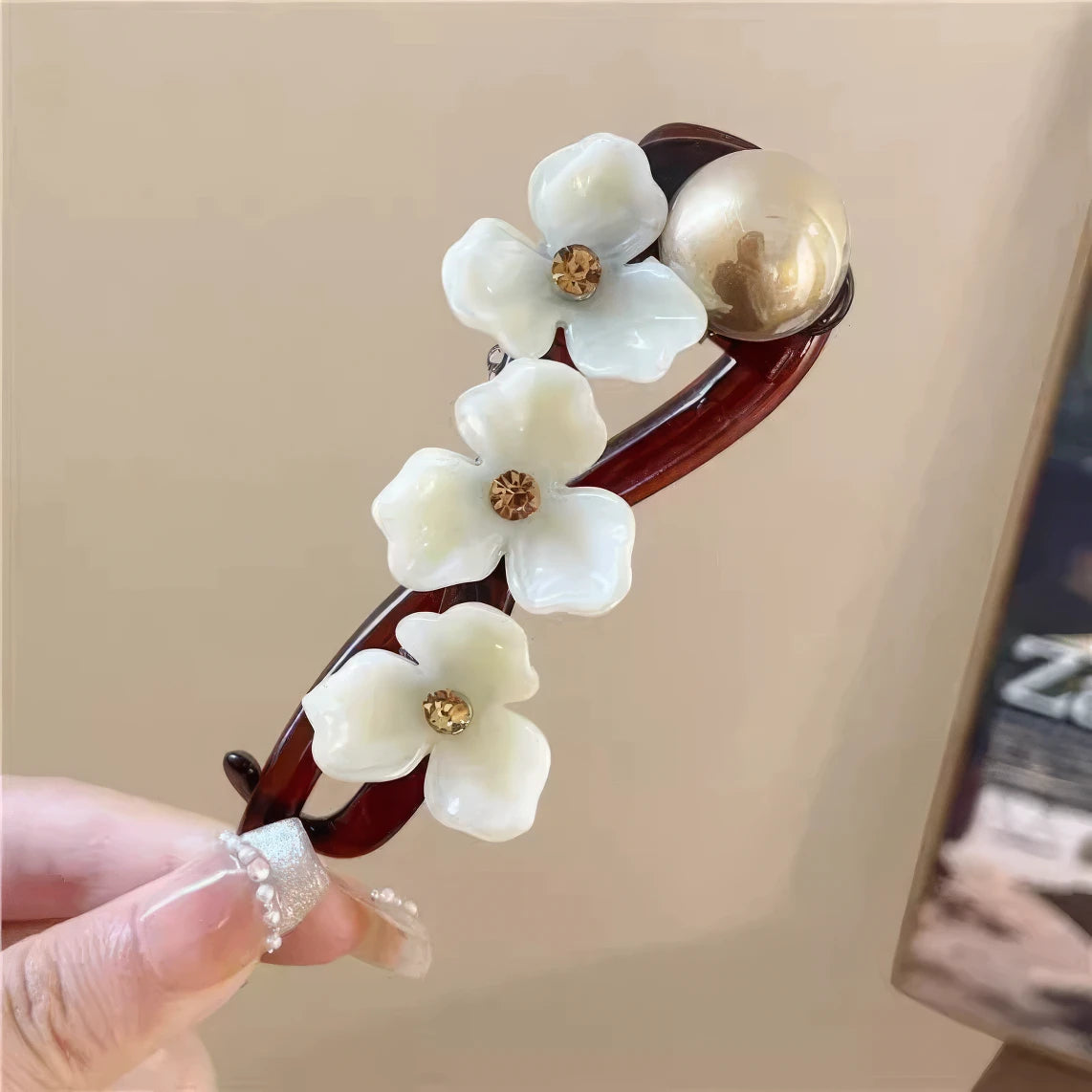 Hand holding French flower twist clip with white flowers and pearl, light background