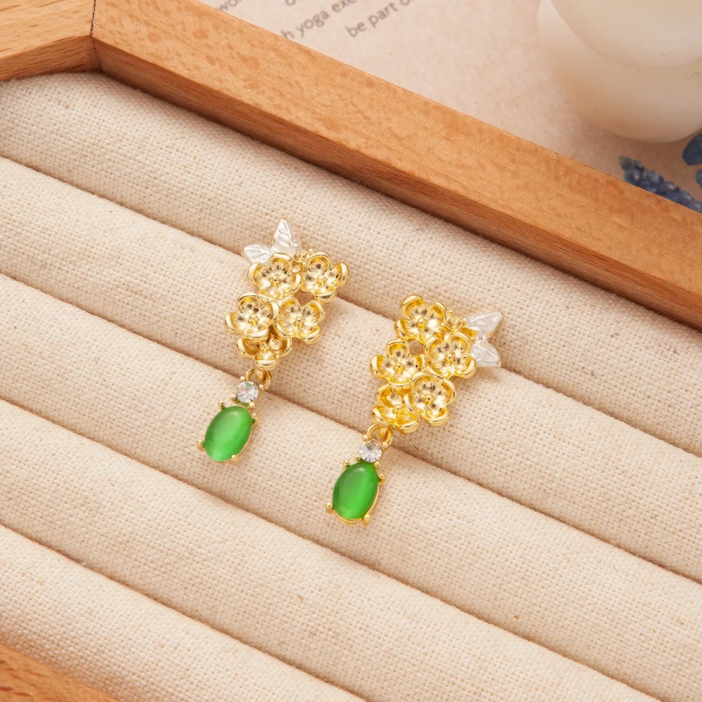 Gold flower earrings with green drops on a beige jewelry tray