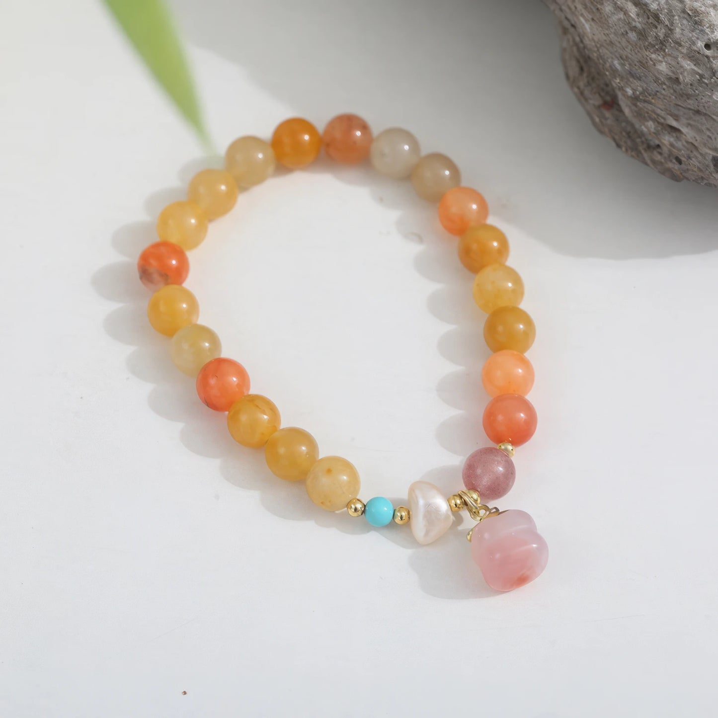 Golden silk jade agate pumpkin bead bracelet with pink pendant on a light surface