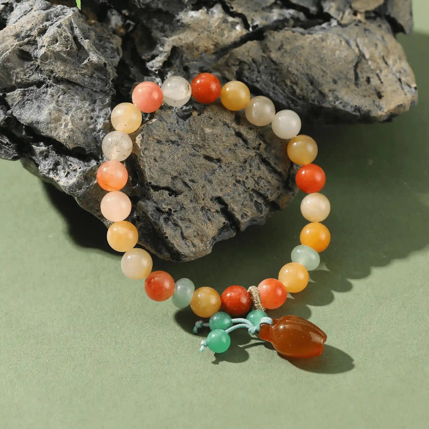 Golden silk jade agate pumpkin bead bracelet with green pendant on a rock background