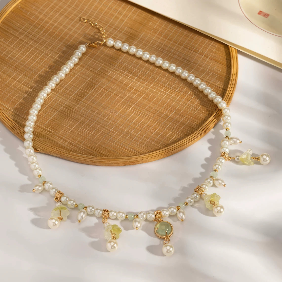 Grass green cabochon lily necklace with pearls, displayed on light surface, full view