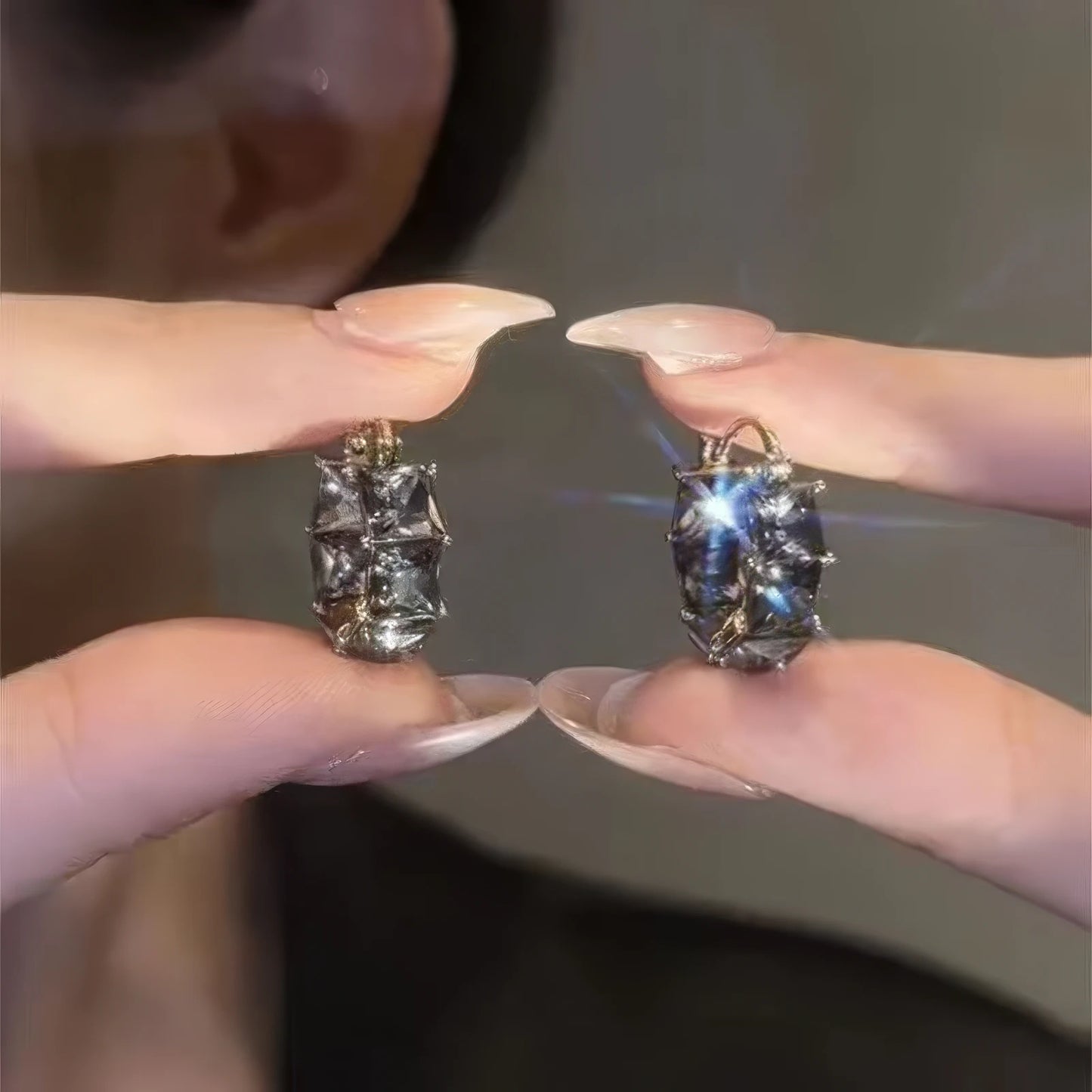 Hands holding gray crystal hoop earrings, showcasing sparkling details