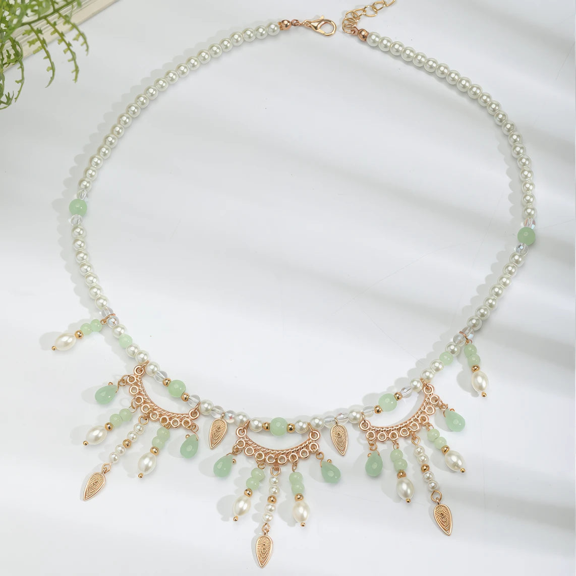 Green multi - hole necklace with pearls and gold details, displayed on light surface, light background