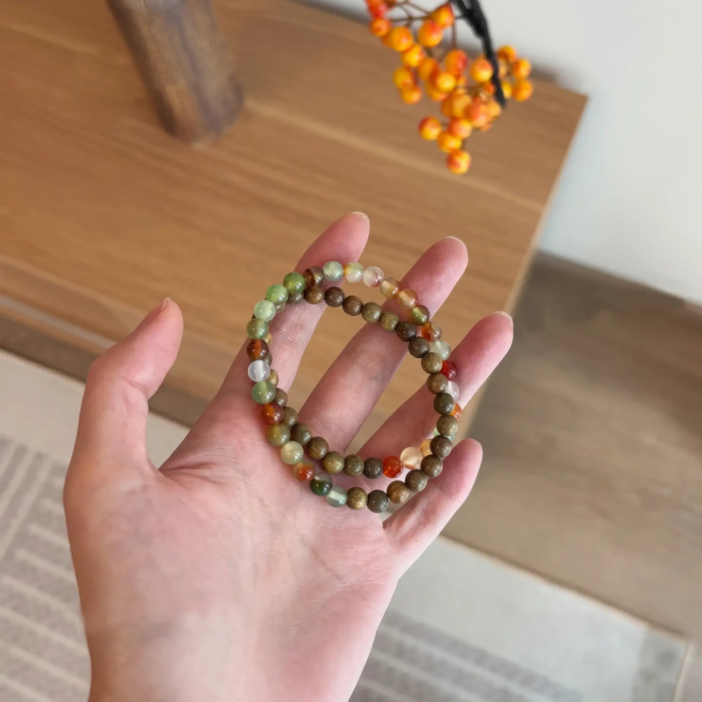 Another hand holding green sandalwood and peacock agate beaded bracelet