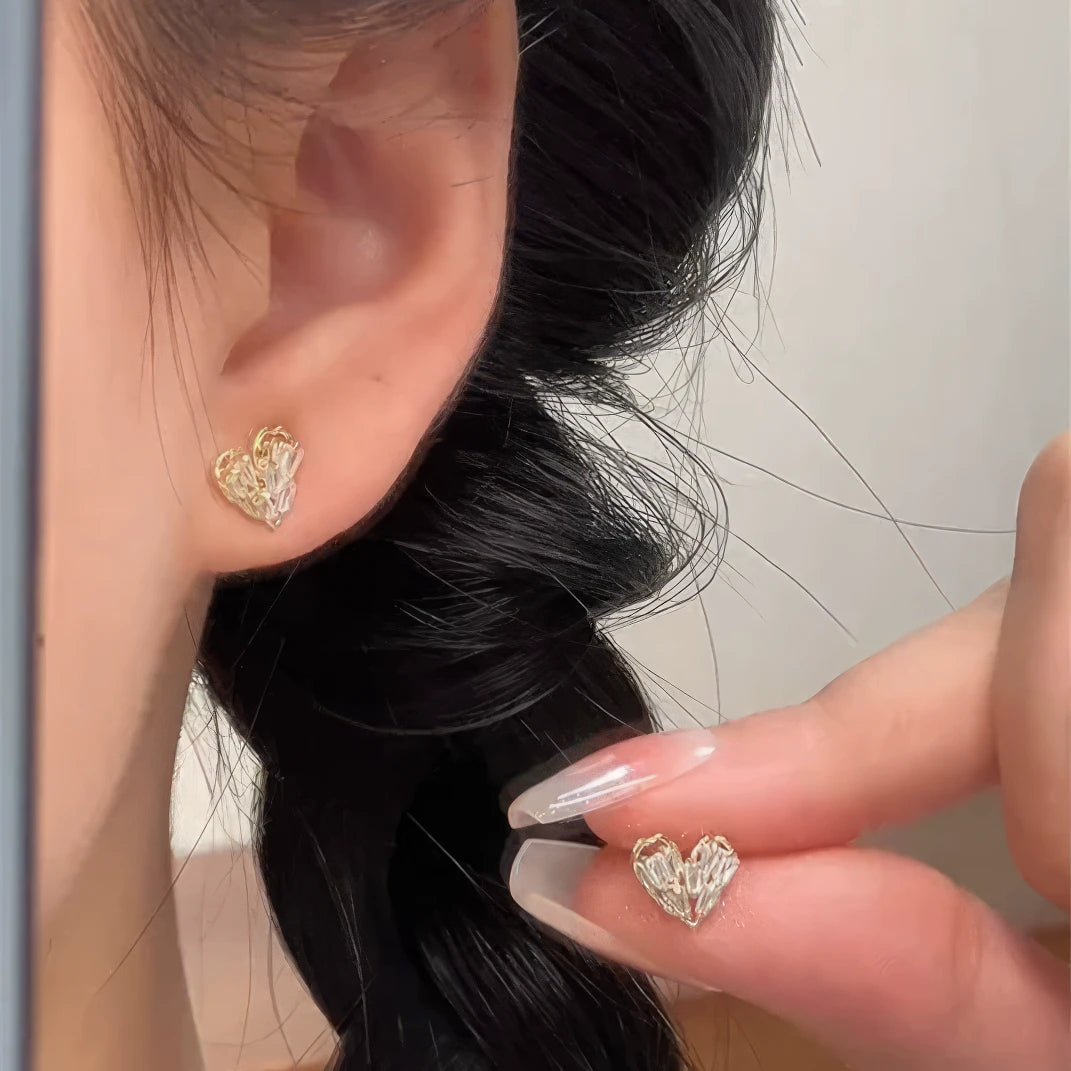 Small heart - shaped earrings worn on ear, hand adjusting, showcasing delicacy