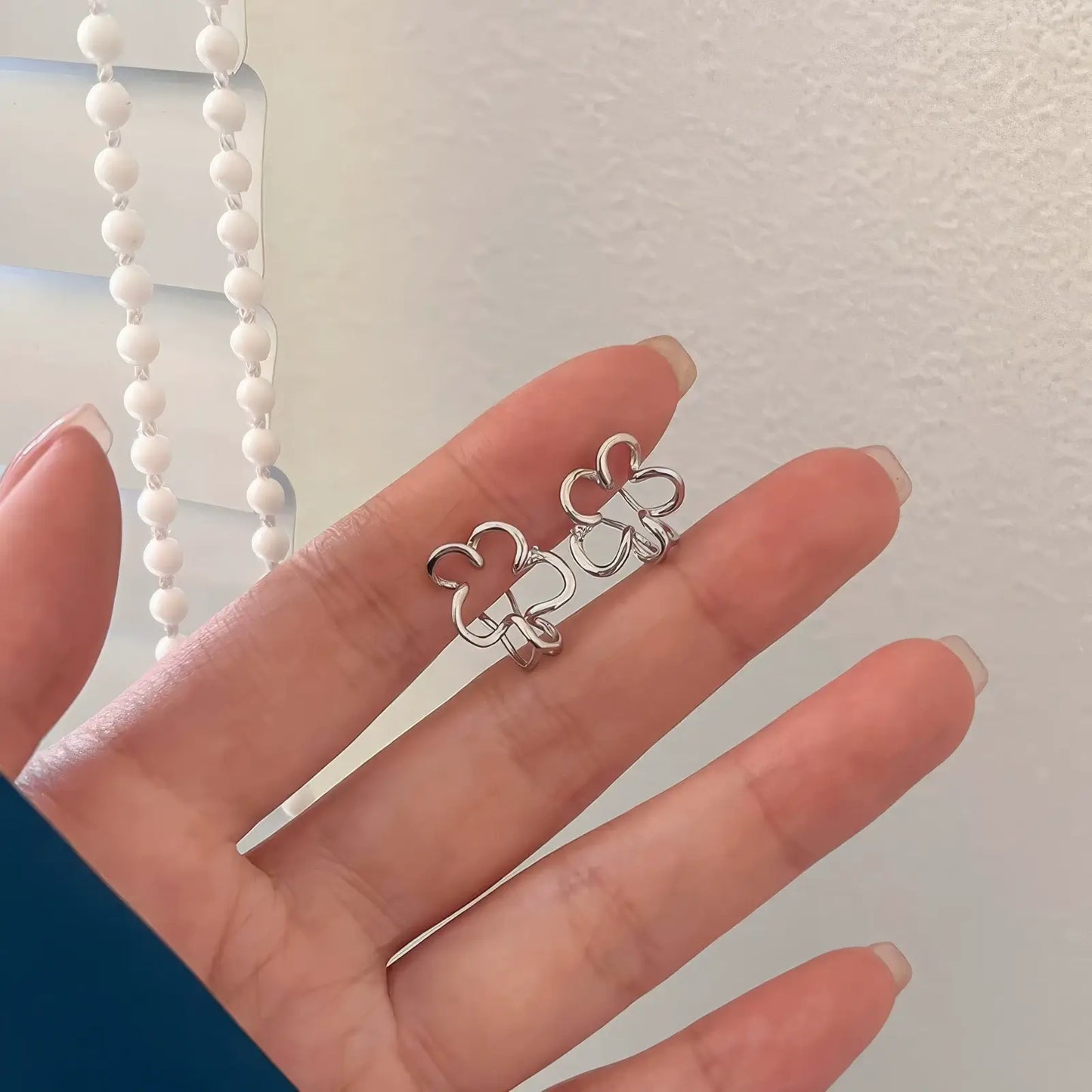 Hand holding irregular flower ear clips, showcasing the unique design with a pearl chain in the background