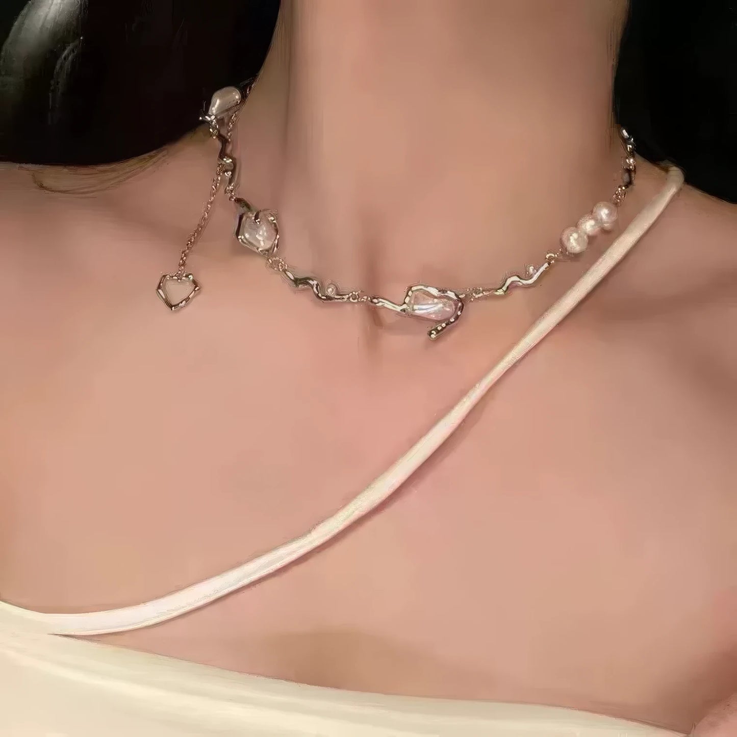 Irregular shaped pearl necklace worn, emphasizing the pendant against a light - colored strap