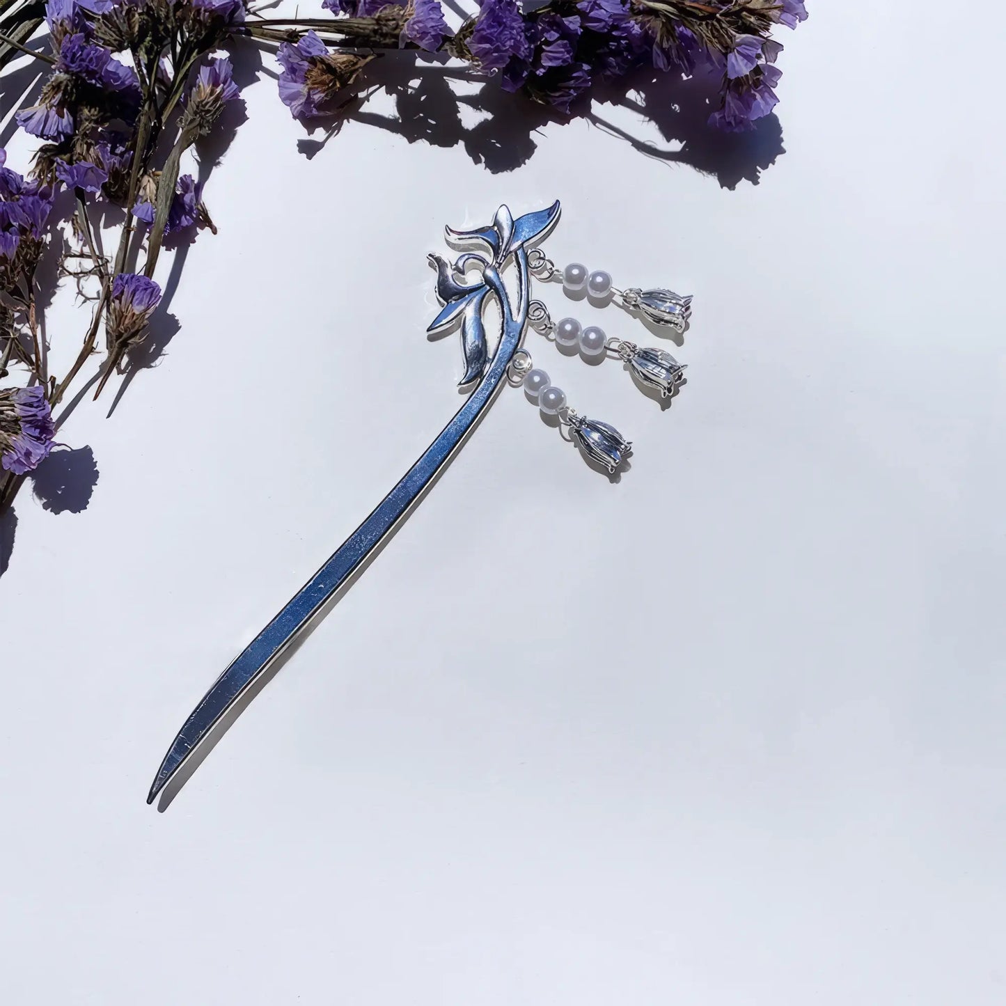 Lily - of - valley hairpin, silver with pearl tassels, against white background with purple flowers